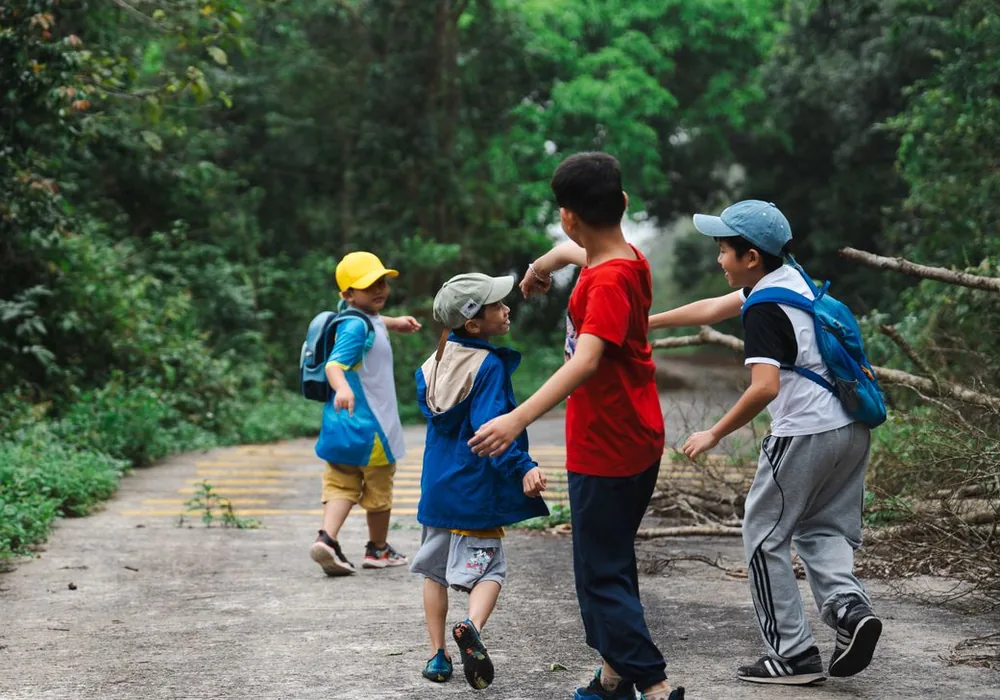 Kinder mit Rucksäcken und eine Betreuungsperson auf einem Waldweg
